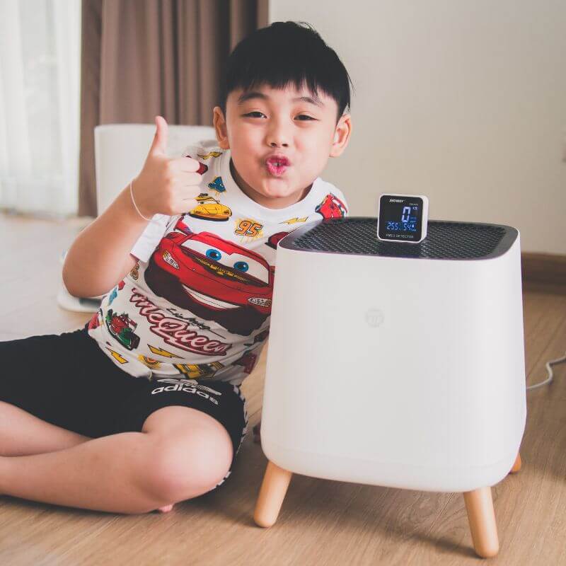 a little asian boy next to a sqair air purifier showing thumbs up