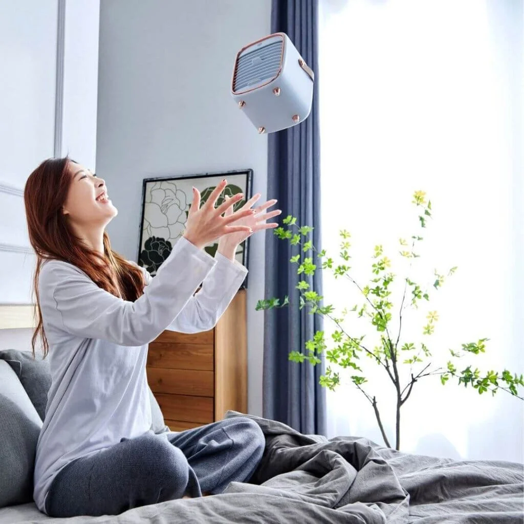 a young woman on the bed smiling throwing a qt3 portable air purifier in the air
