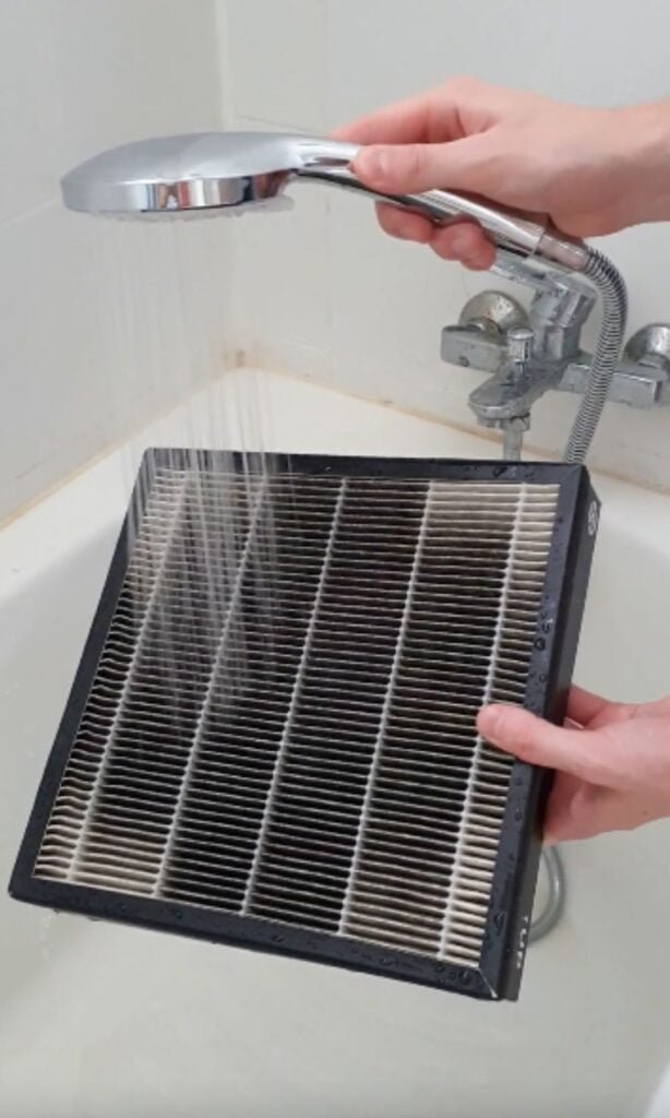 a hand holding a shower head to wash a hepa filter