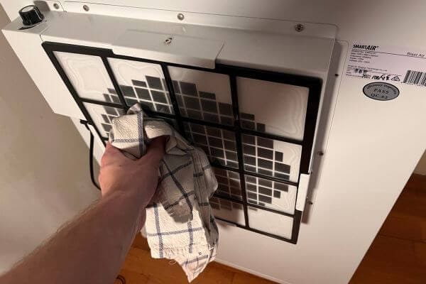 a photo of a males hand cleaning the pre-filter of an air purifier with a cloth