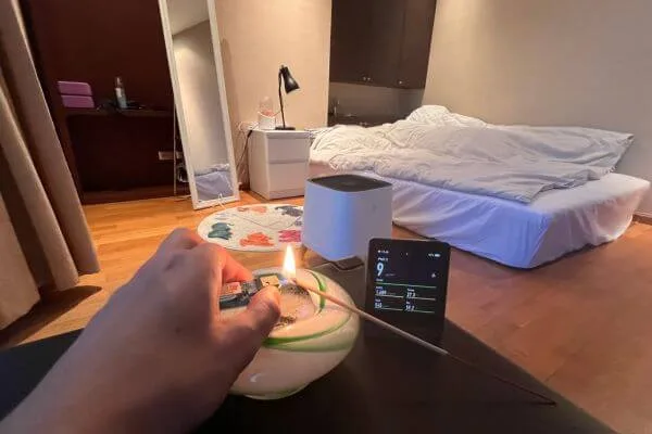 an air purifier in a bedroom next to an air quality monitor and a lit incense stick